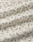 A close-up of a draped fabric with a delicate floral pattern in muted pink and olive green on an off-white background.