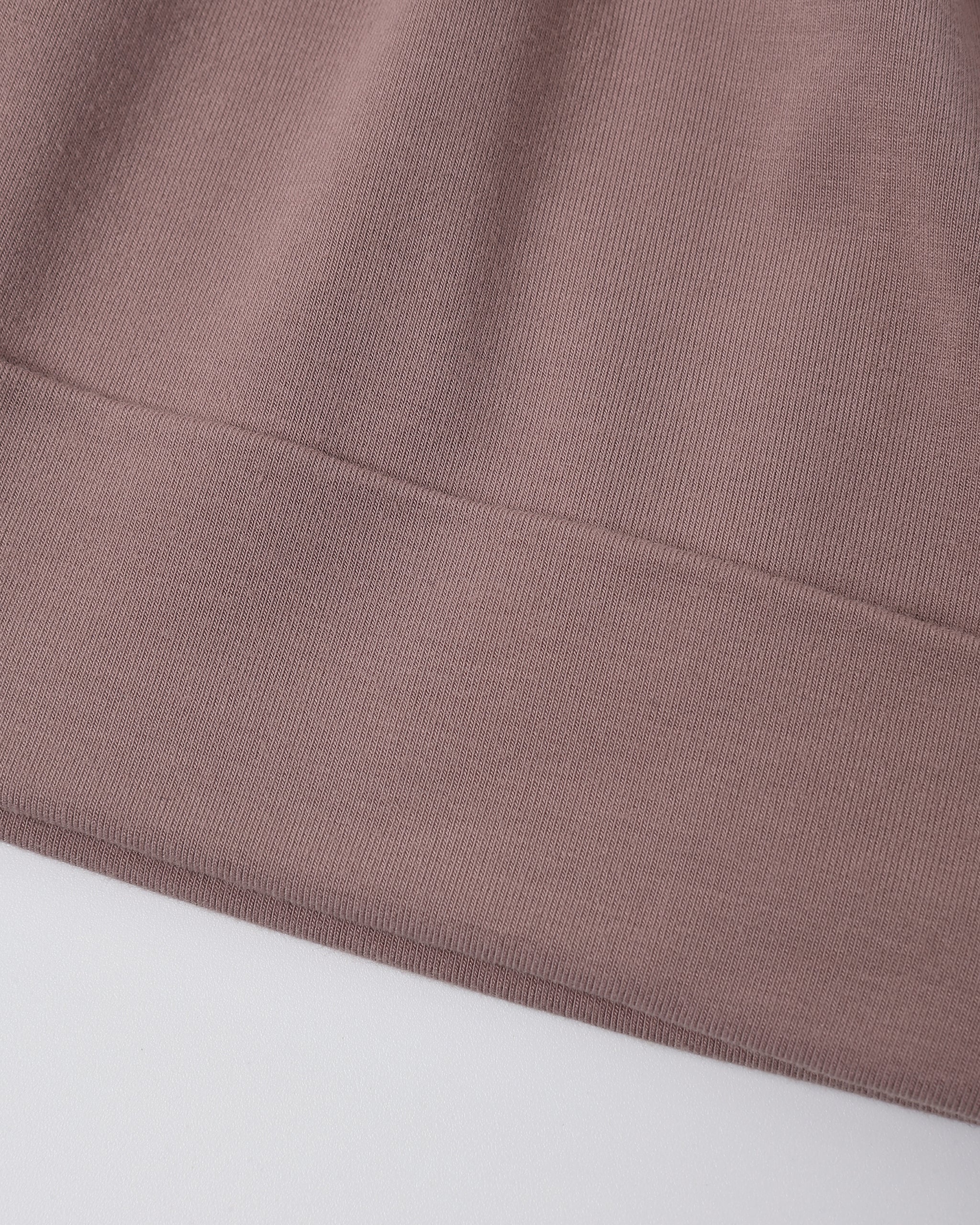 Close-up of a ribbed knit fabric in a muted dusty mauve-pink color, showing the texture and a folded hem against a plain light background.
