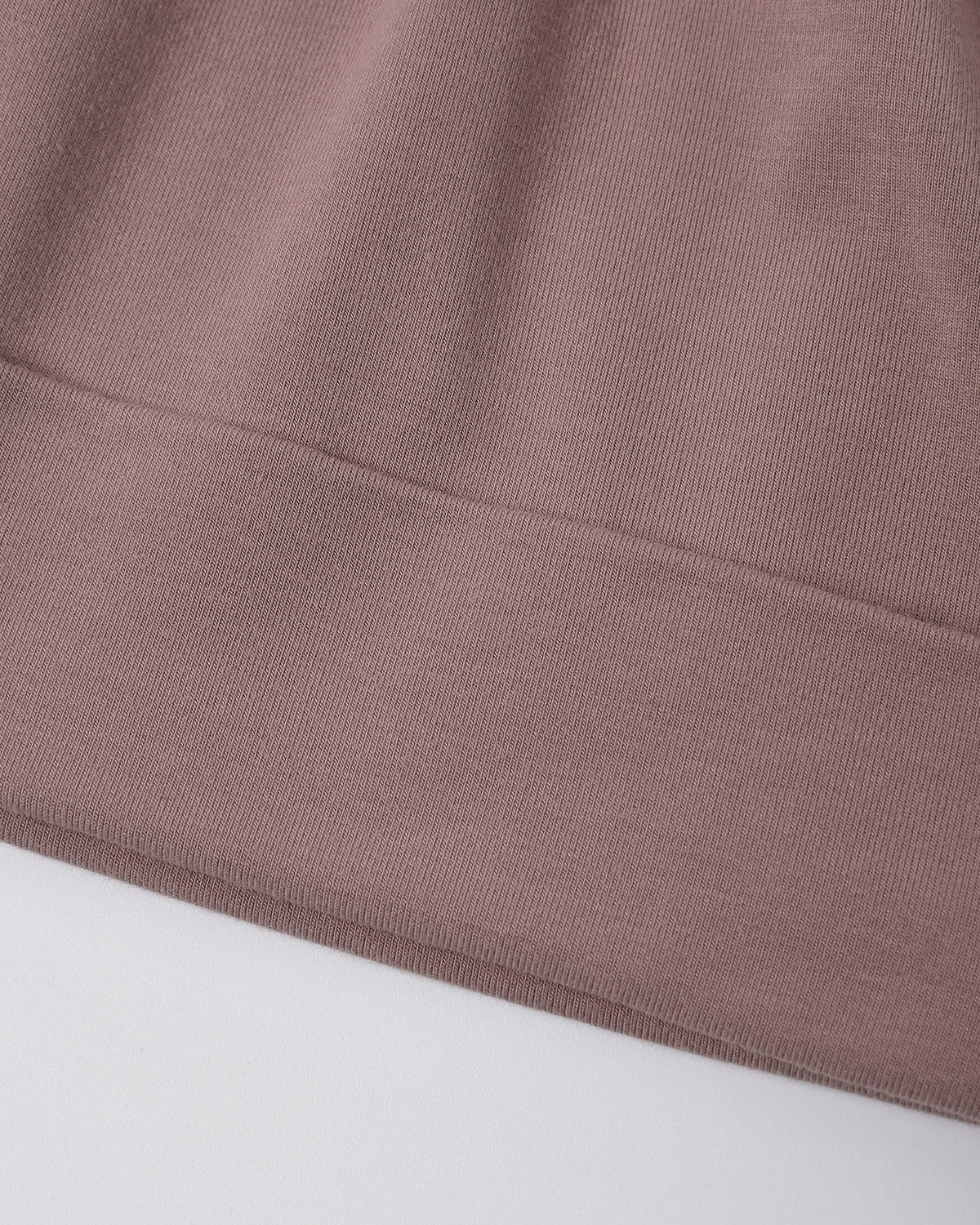 Close-up of a ribbed knit fabric in a muted dusty mauve-pink color, showing the texture and a folded hem against a plain light background.