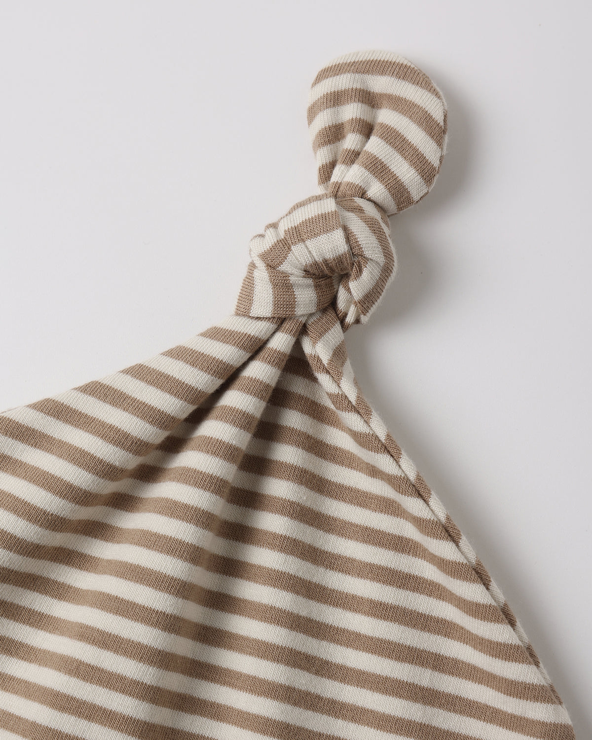 A close-up of a soft fabric baby lovey or comforter with horizontal brown and cream stripes, tied in a knot at the top against a light gray background.