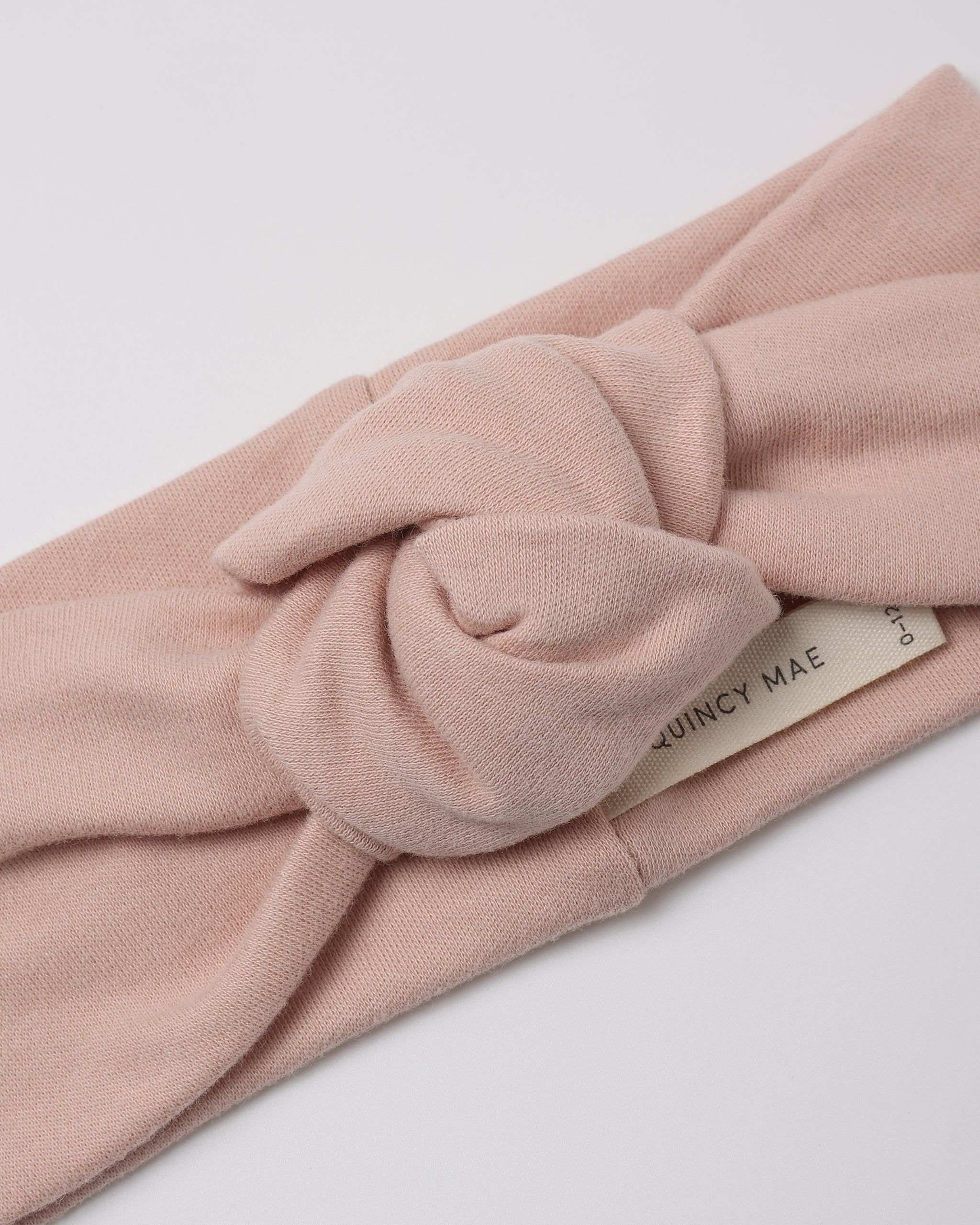 A dusty pink knotted fabric headband with a cream-colored brand tag reading 'QUINCY MAE' on a clean white background.