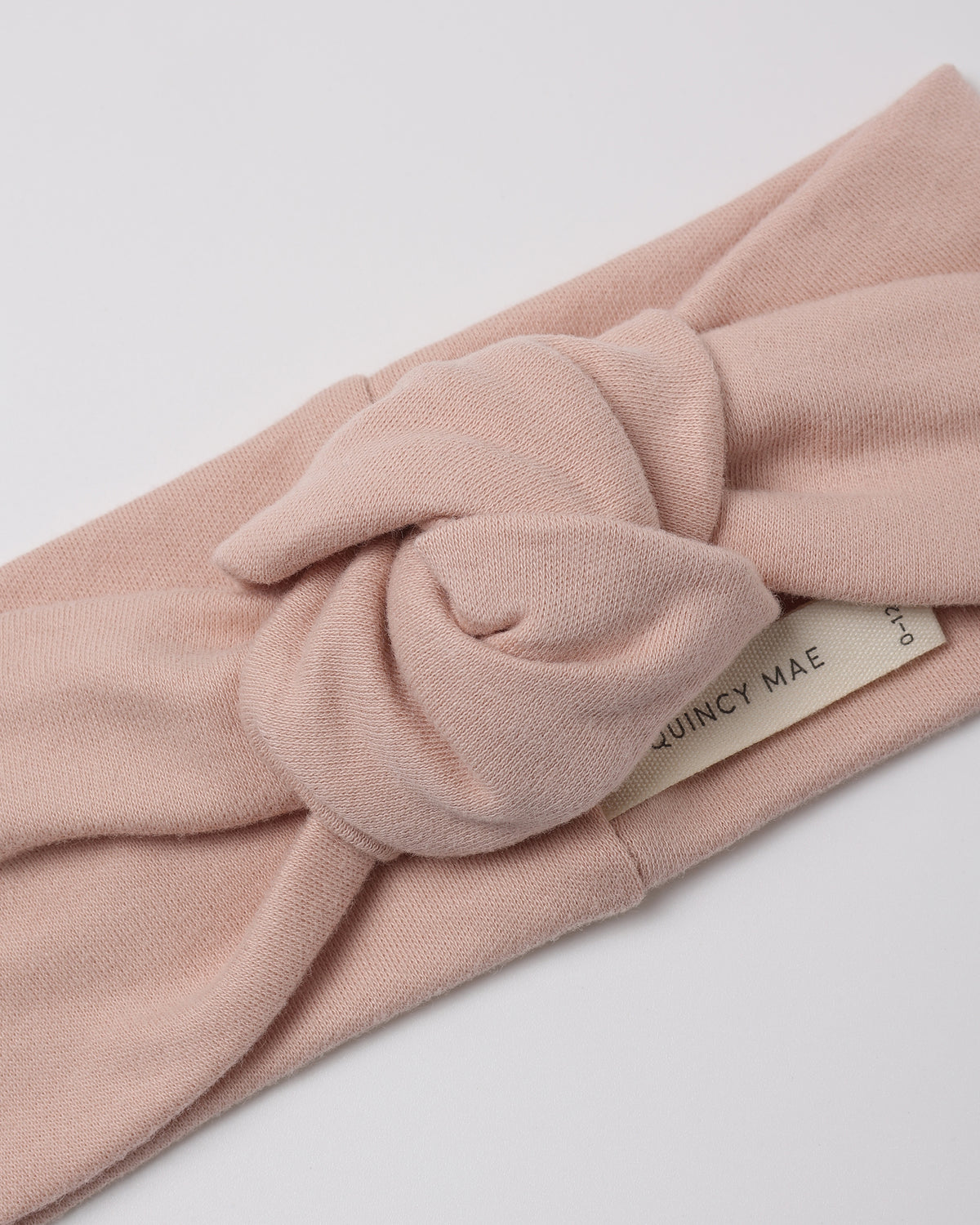 A dusty pink knotted fabric headband with a cream-colored brand tag reading 'QUINCY MAE' on a clean white background.