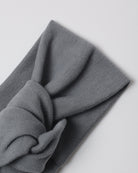 A folded dark gray knit headband with a twisted knot detail, shown on a light gray background.