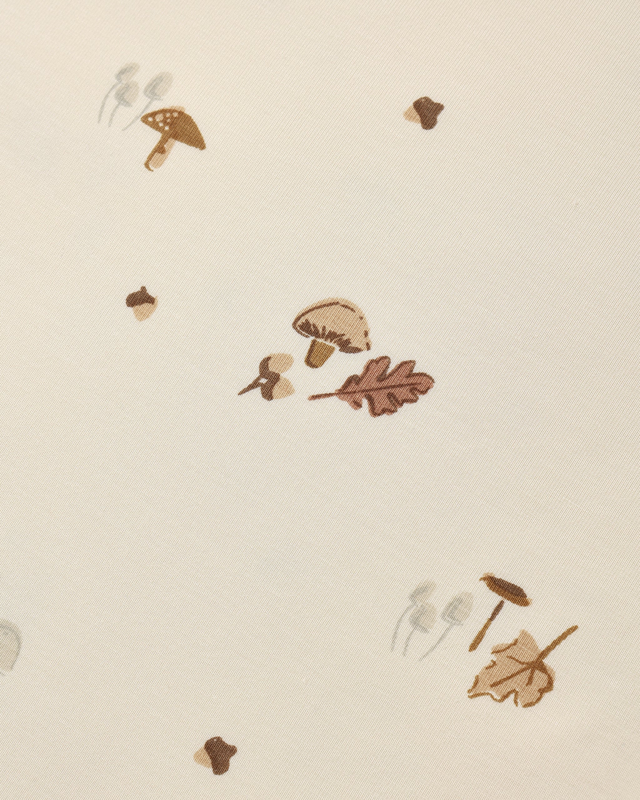 A close-up of a cream-colored surface with a scattered autumn-themed pattern featuring brown mushrooms, acorns, and oak leaves.