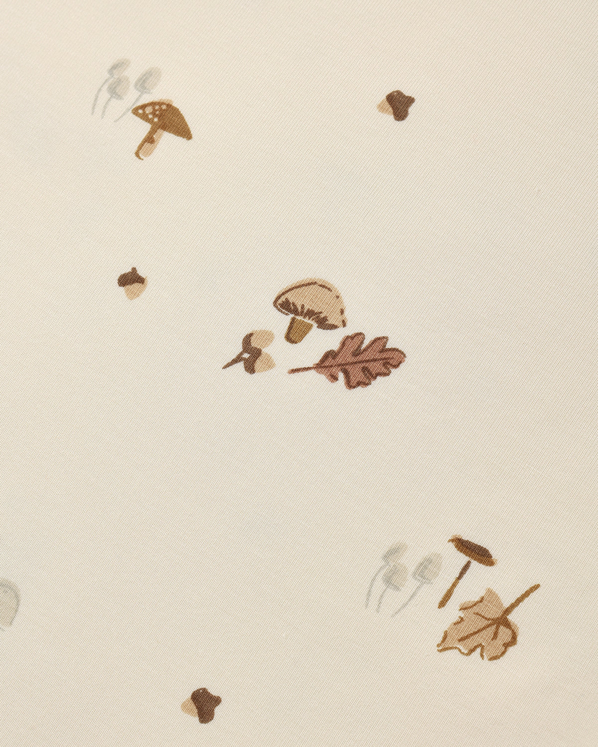 A close-up of a cream-colored surface with a scattered autumn-themed pattern featuring brown mushrooms, acorns, and oak leaves.
