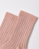 A close-up of a pair of ribbed ankle socks in a soft dusty pink color, showing the knit texture and cuff details against a clean white background.