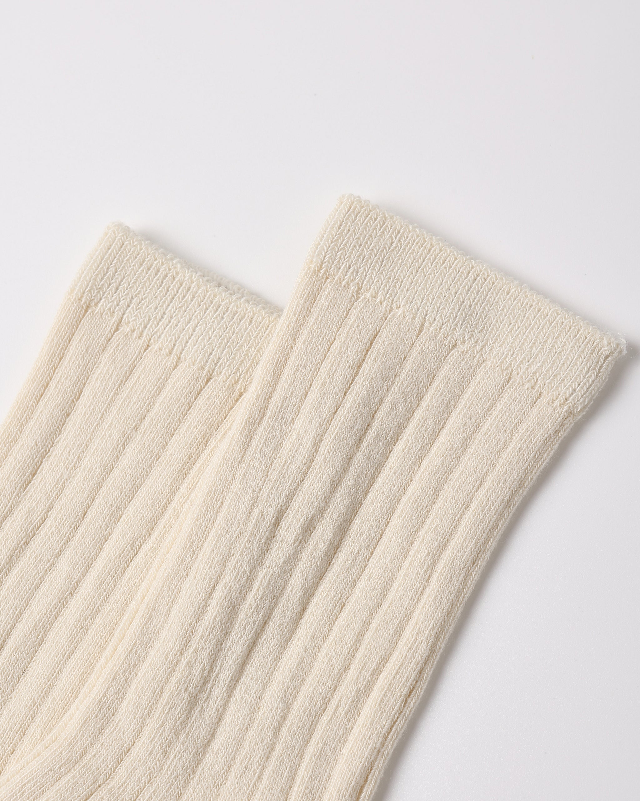 A close-up of a pair of ribbed cream-colored socks on a light gray background.