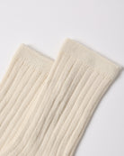 A close-up of a pair of ribbed cream-colored socks on a light gray background.