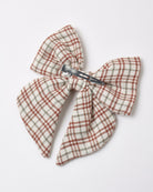 A children's hair bow featuring a red, white, and brown plaid pattern with a metal alligator clip attached to the back.