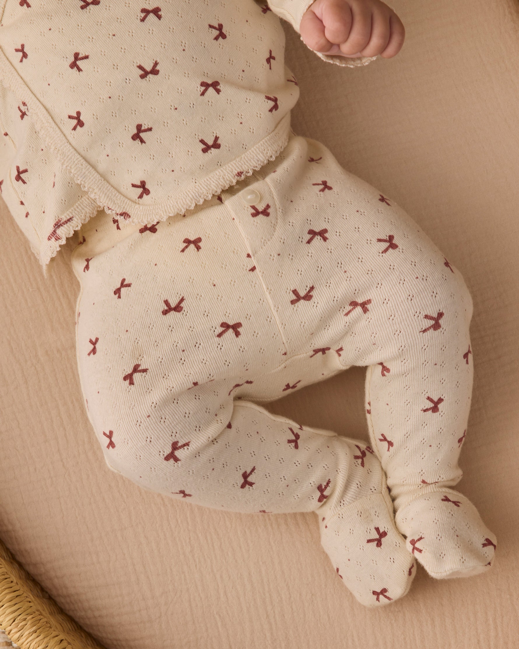 Close-up of an infant's legs and torso wearing the Quincy Mae red bows print long-sleeve top and footed pants.