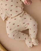 Close-up of an infant's legs and torso wearing the Quincy Mae red bows print long-sleeve top and footed pants.
