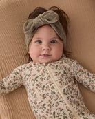A baby wearing a sage green velour bow headband by Quincy Mae and a floral print organic cotton sleeper.