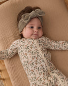A baby wearing a sage green velour bow headband by Quincy Mae and a floral print organic cotton sleeper.