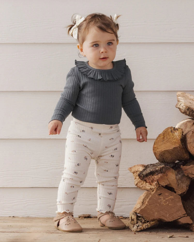 A toddler wearing a grey Rylee + Cru ruffle-collar long-sleeve top paired with cream-colored ditsy floral ribbed leggings.