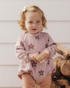 A toddler wearing the Rylee + Cru Daisy Crew Neck Romper in a soft pink hue with an all-over dark floral print.
