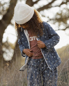 A child wearing a matching blue patterned pajama set with a white knit beanie, standing outdoors in a grassy field.
