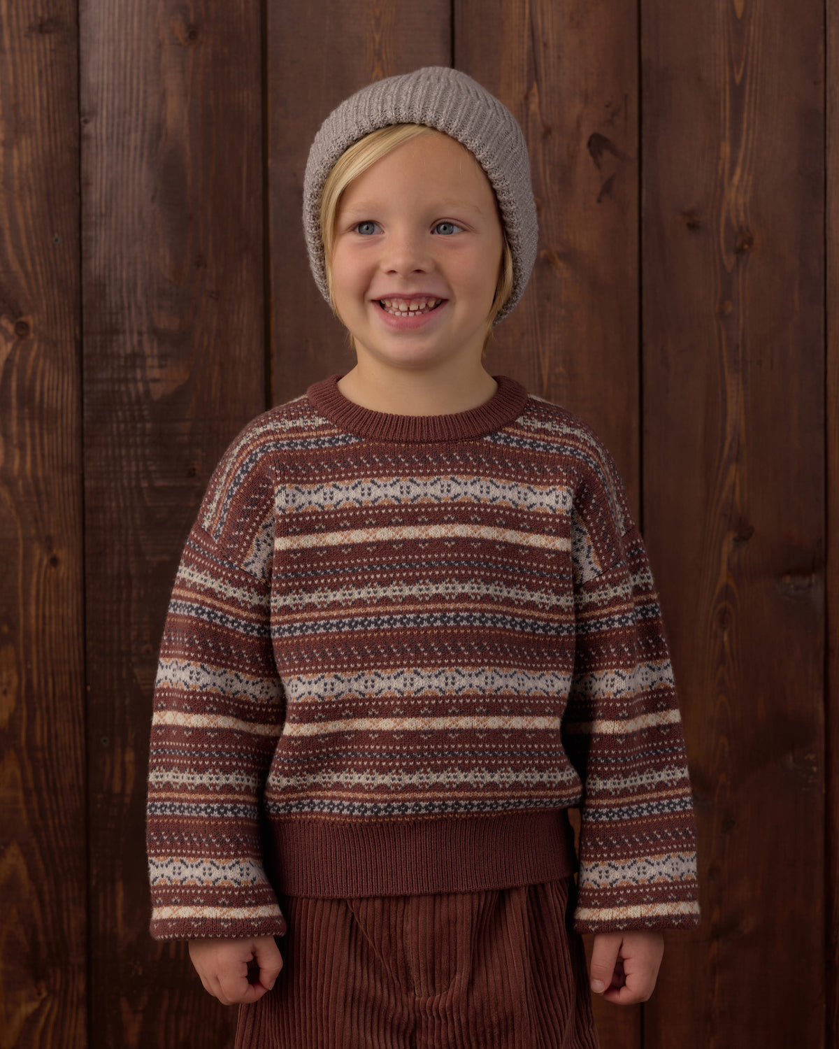 Child wearing a patterned sweater and knit hat against a wooden background
