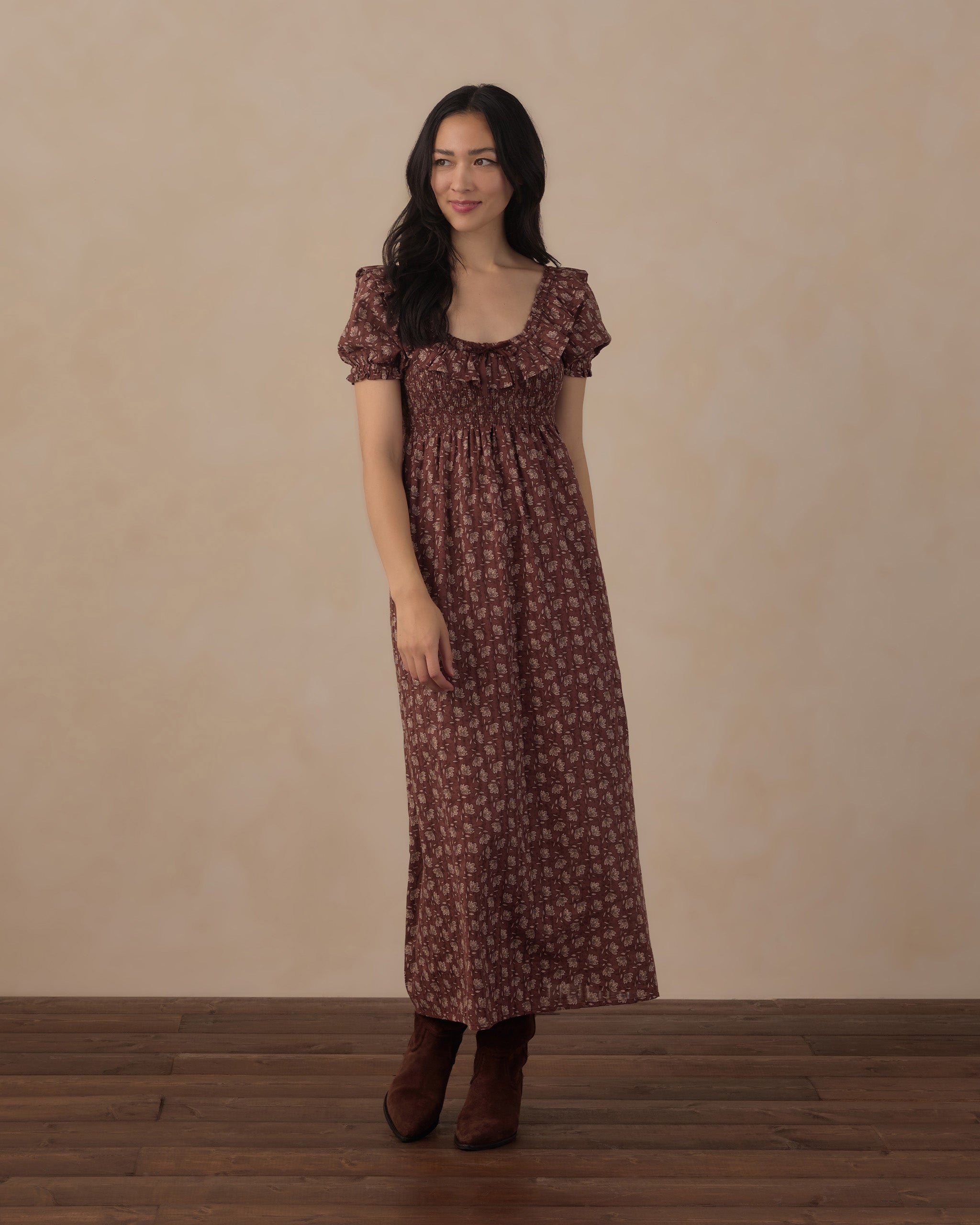 Woman wearing a brown floral dress against a beige background