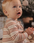 A close-up of a baby wearing a cream-colored long-sleeve romper with thin rust-brown horizontal stripes, looking off-camera with an open mouth.