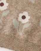 Close-up of a knit sweater showing a floral pattern in cream, sage green, and brown on a heathered taupe-beige background.