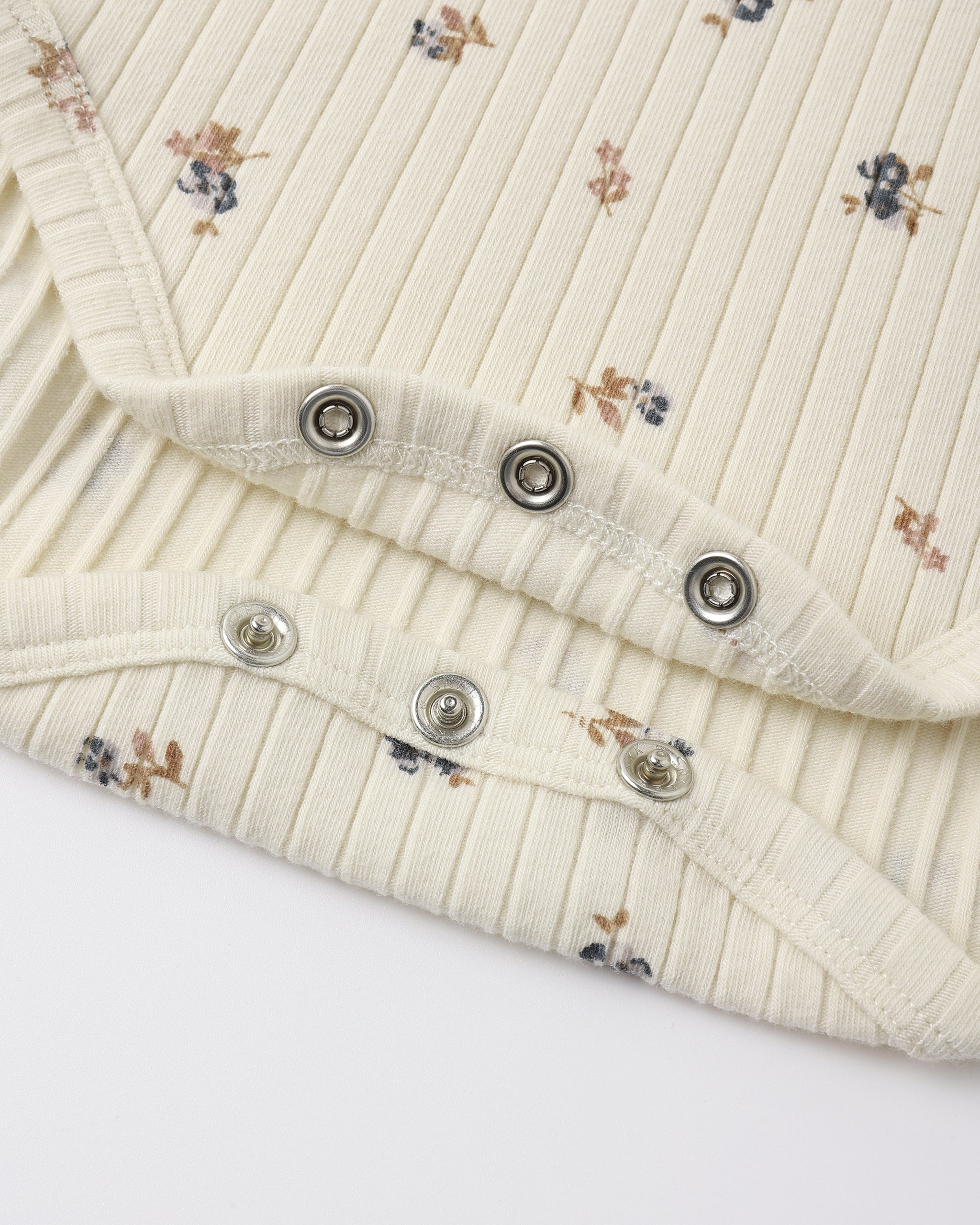 Close-up of a cream-colored ribbed knit garment with a small floral print, featuring silver metal snap buttons along the folded edge.