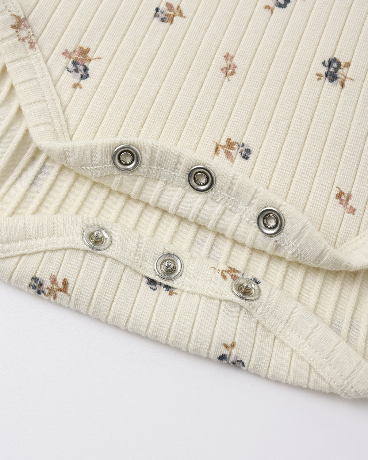 Close-up of a cream-colored ribbed knit garment with a small floral print, featuring silver metal snap buttons along the folded edge.
