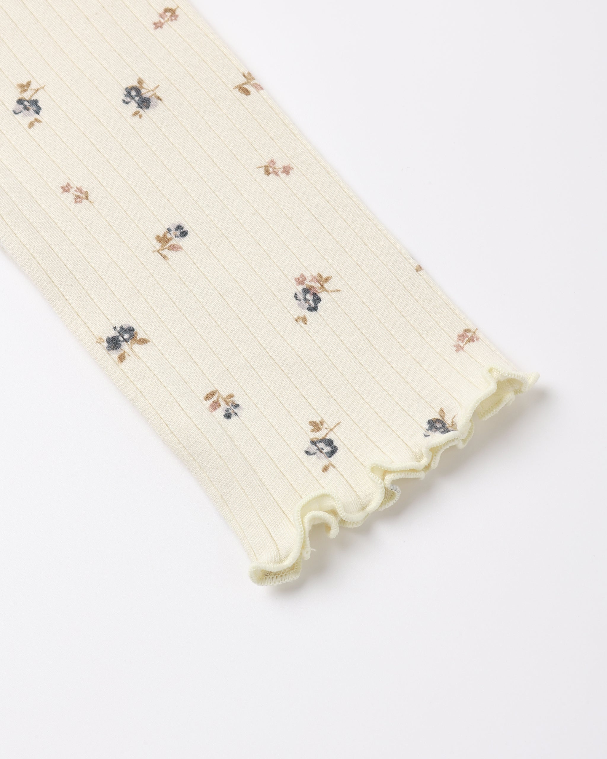 A close-up of a ribbed cream-colored sleeve or cuff featuring a delicate, small-scale floral print in muted blue and brown, finished with a ruffled edge.
