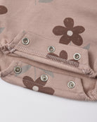Close-up of a dusty pink fabric garment with a brown floral print and silver metal snap buttons.