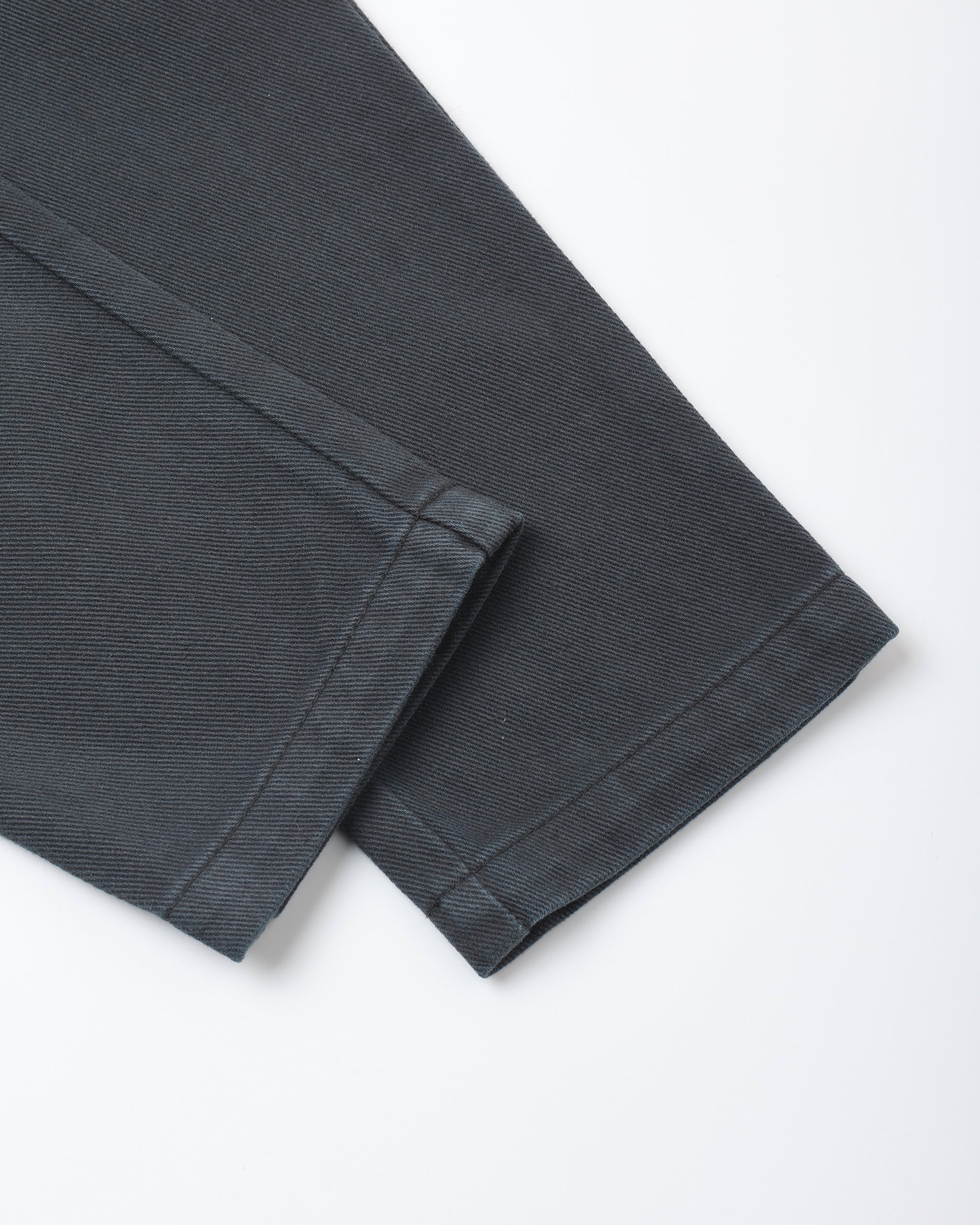 A close-up of folded dark charcoal gray fabric, showing the texture and hem detail against a clean white background.