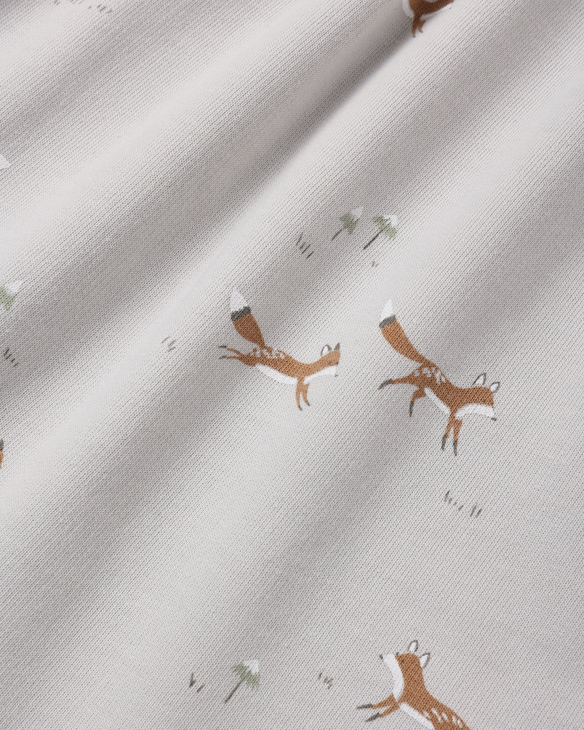 Close-up of a light cream fabric with a repeating print of brown foxes and small white flowers.