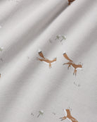 Close-up of a light cream fabric with a repeating print of brown foxes and small white flowers.