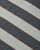 A close-up of a striped textile pattern featuring diagonal bands of dark charcoal gray, light beige, and thin rust-red lines.