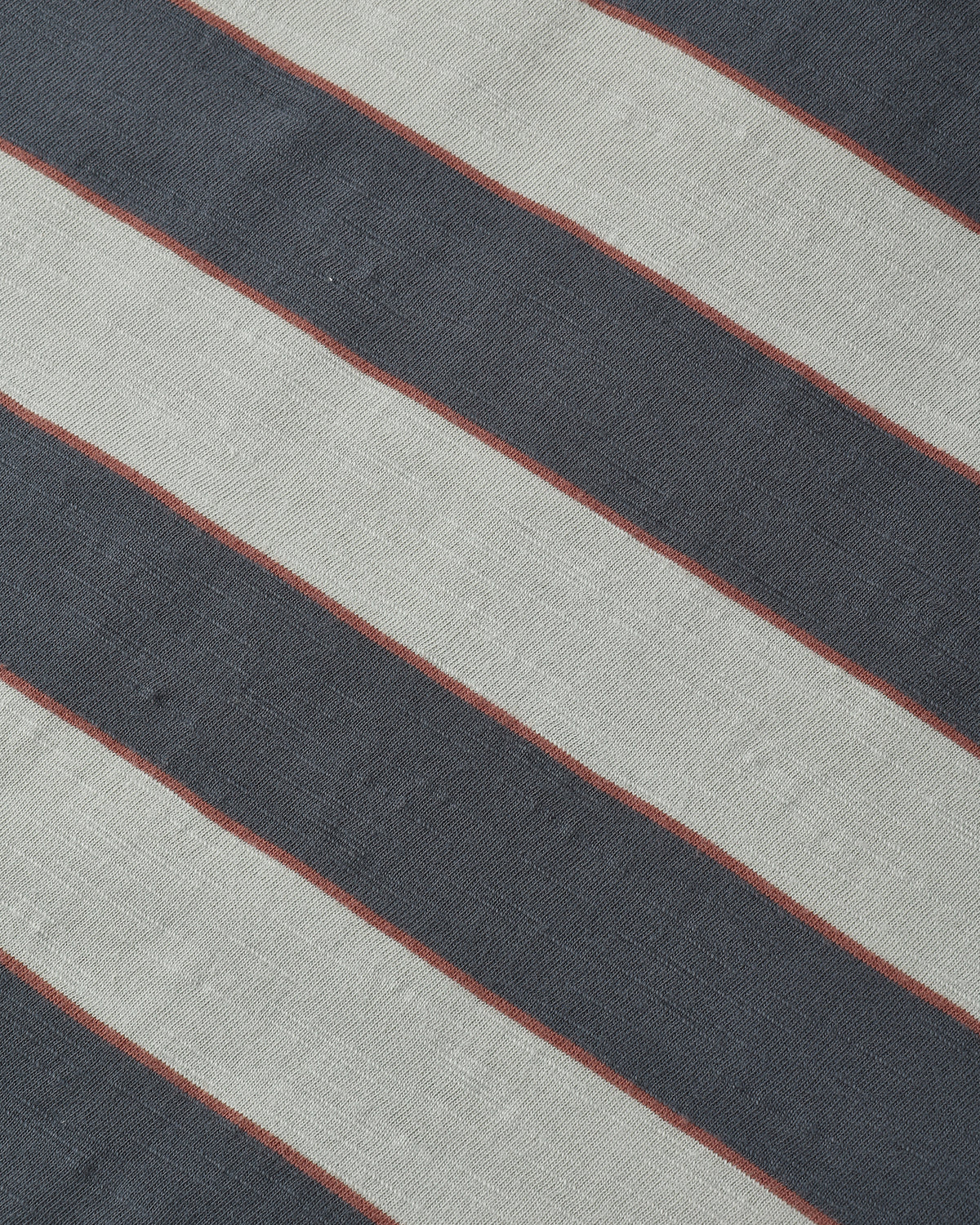 A close-up of a striped textile pattern featuring diagonal bands of dark charcoal gray, light beige, and thin rust-red lines.