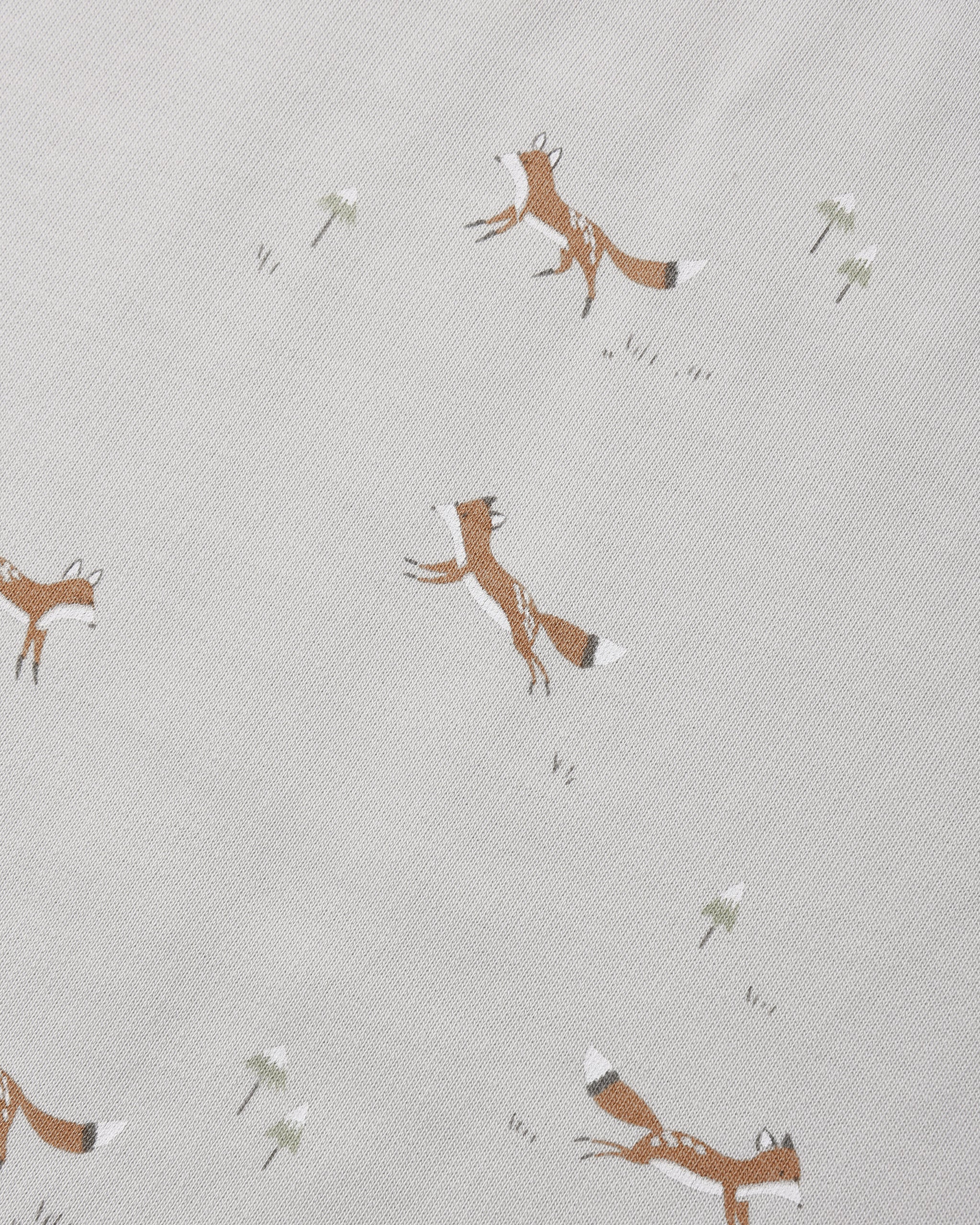 A close-up of a light beige fabric with a repeating pattern of brown foxes and small white flowers.