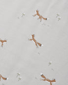 A close-up of a light beige fabric with a repeating pattern of brown foxes and small white flowers.
