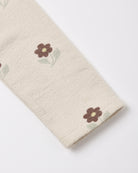 Close-up of a cream-colored textured fabric, likely a sweater or knit garment, featuring a small brown and green embroidered flower pattern.