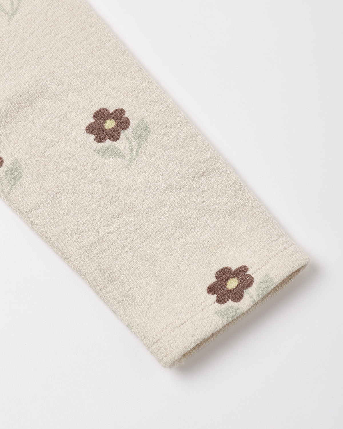 Close-up of a cream-colored textured fabric, likely a sweater or knit garment, featuring a small brown and green embroidered flower pattern.