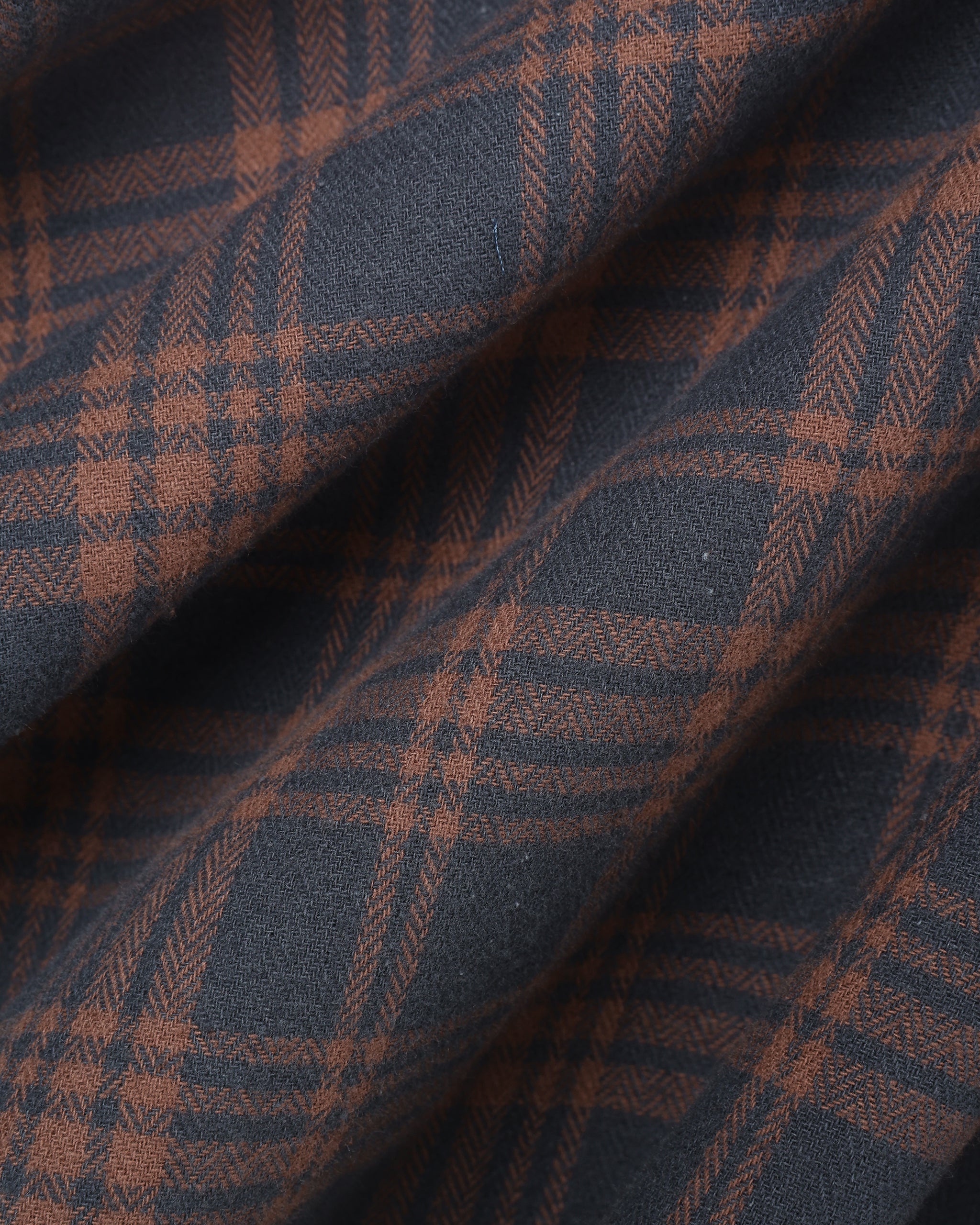 A close-up of a plaid fabric with a dark slate blue base and rust-brown intersecting stripes, showing a textured woven pattern with soft folds.