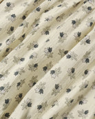 A close-up of a cream-colored fabric with a delicate, repeating floral block print in black and gray, featuring fine vertical stitched stripes.