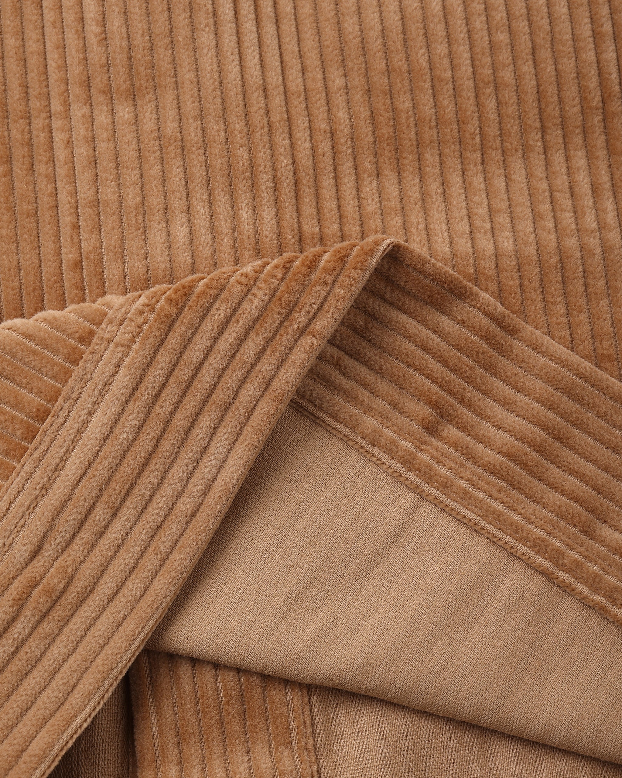 Close-up of a brown corduroy fabric with a folded corner revealing a lighter tan lining.