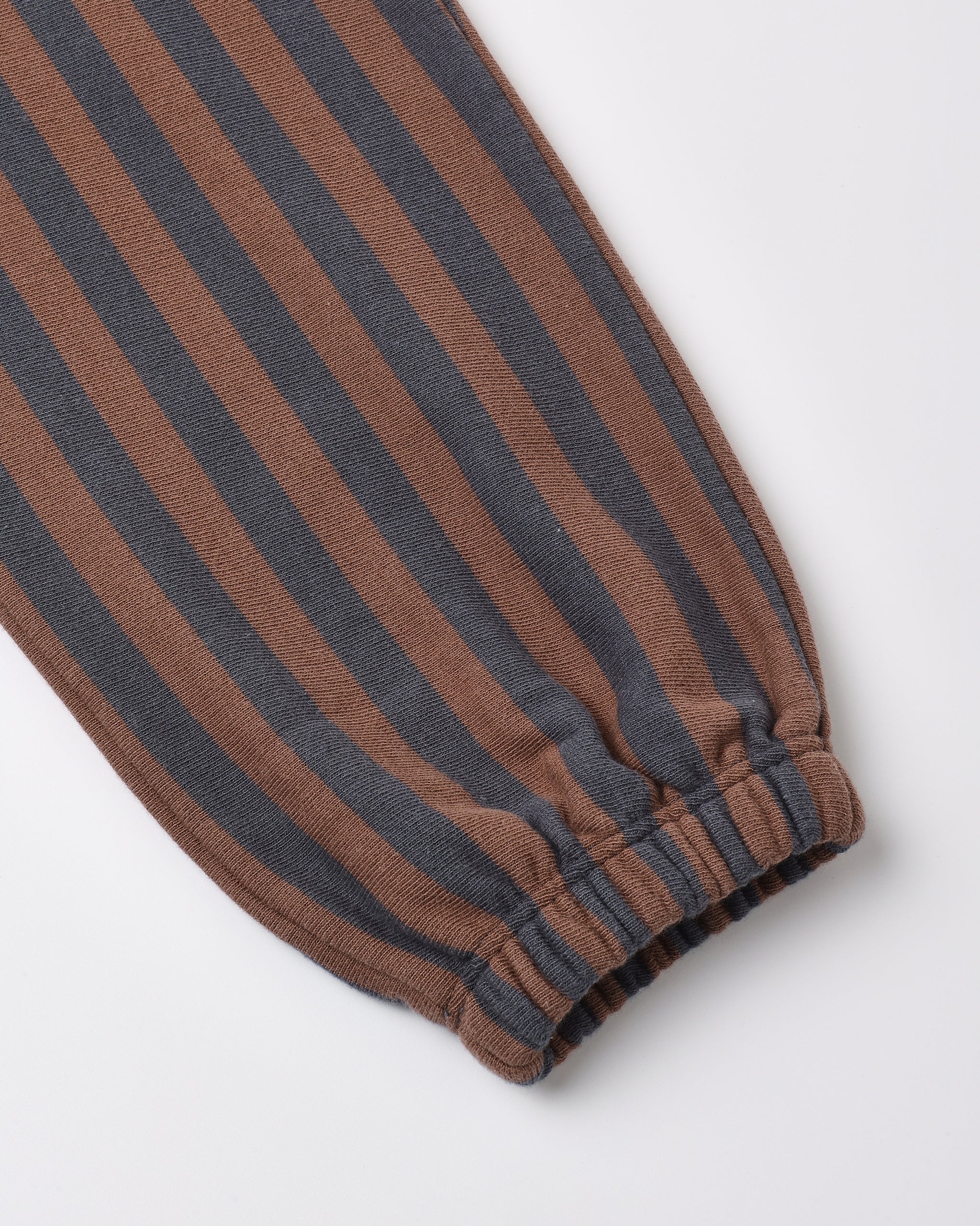 A close-up of a striped fabric product, likely a sweatshirt sleeve or pants leg, featuring alternating brown and dark charcoal gray vertical stripes with a gathered elastic cuff.