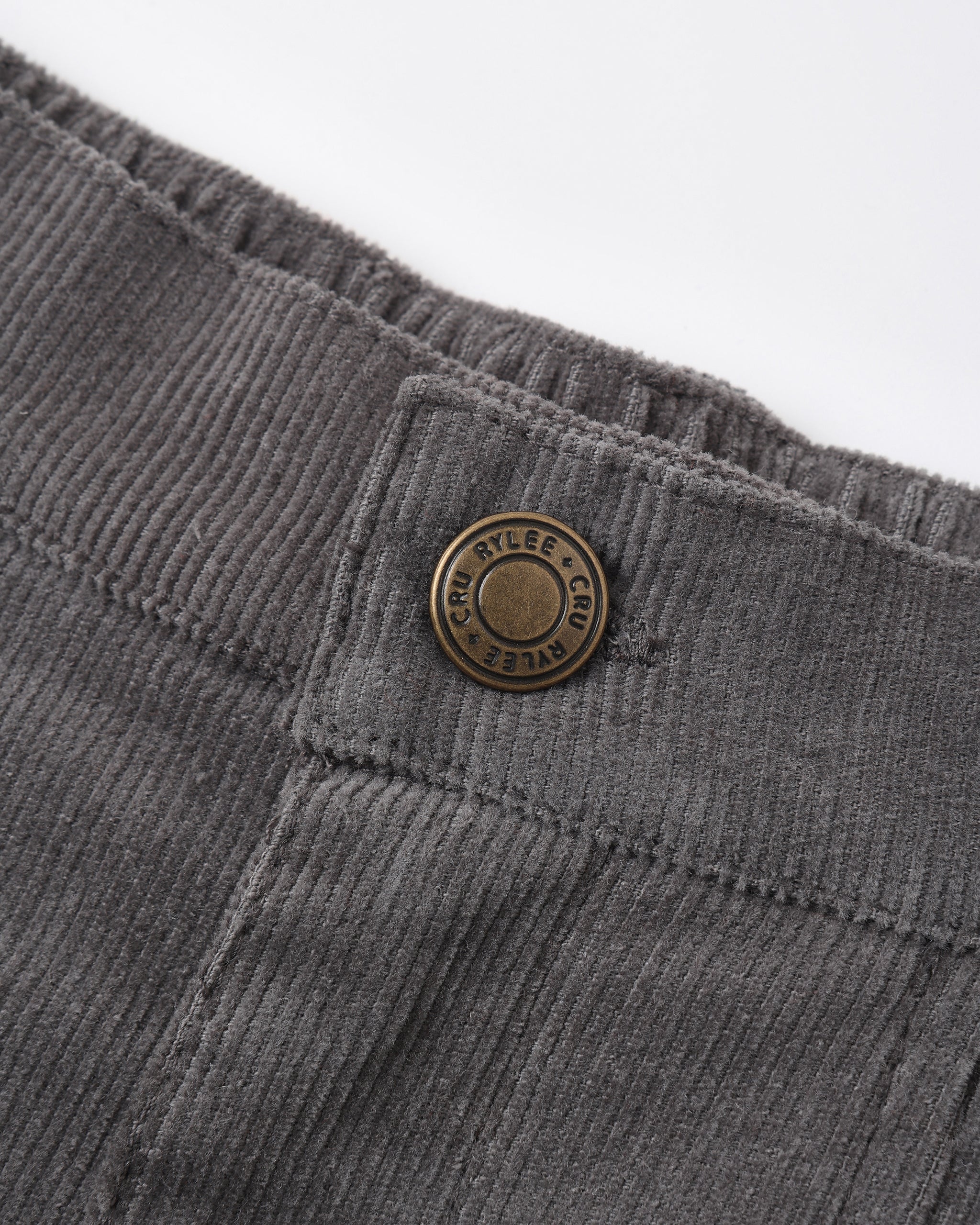 Close-up of dark gray corduroy trousers showing the waistband, button closure, and ribbed fabric texture against a white background.