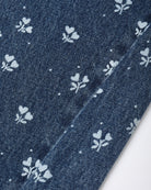 A close-up of dark blue denim fabric with a repeating white floral print and a diagonal seam.