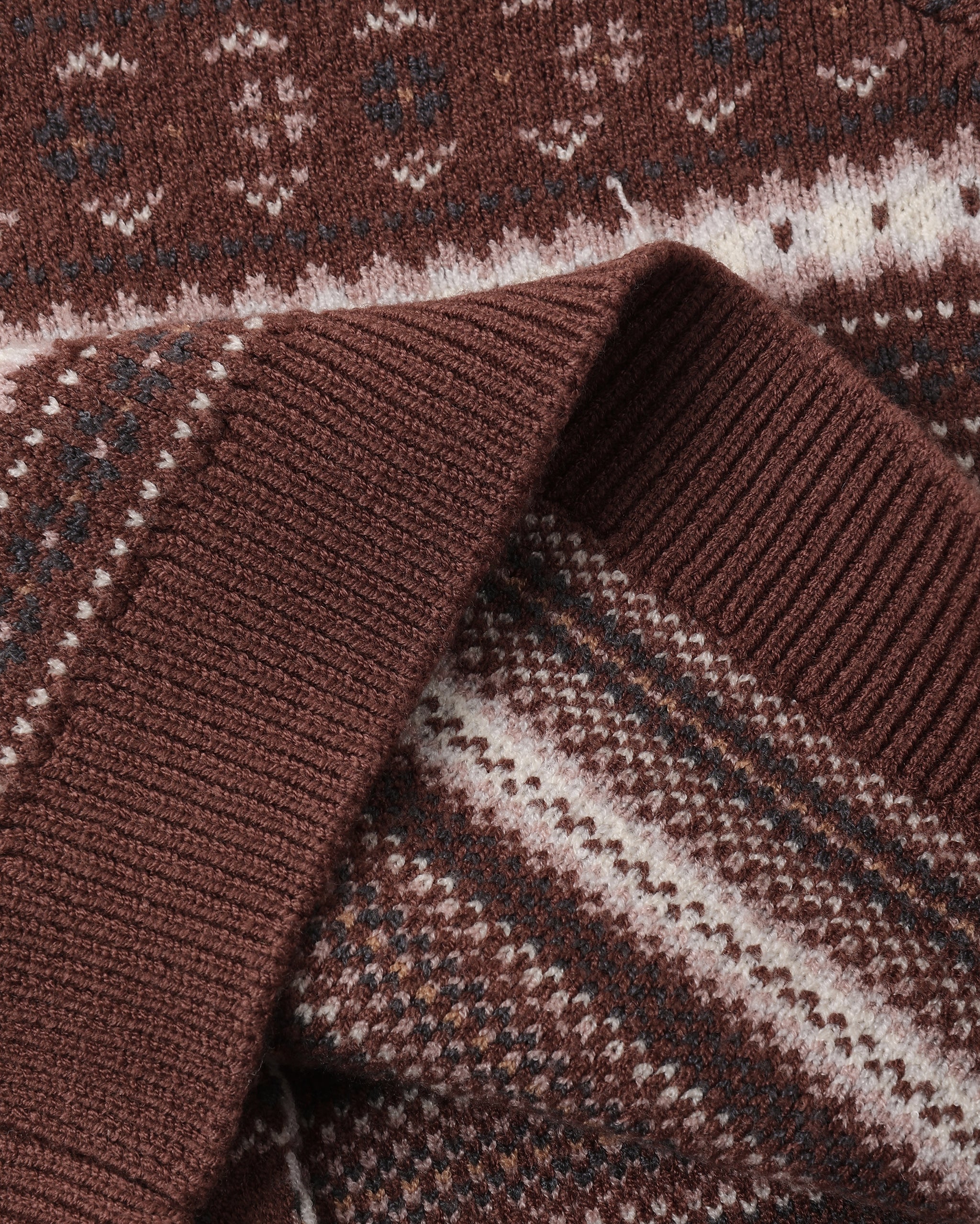 Close-up of a knit sweater showing a ribbed brown collar and a brown, cream, and dark gray Fair Isle patterned body.
