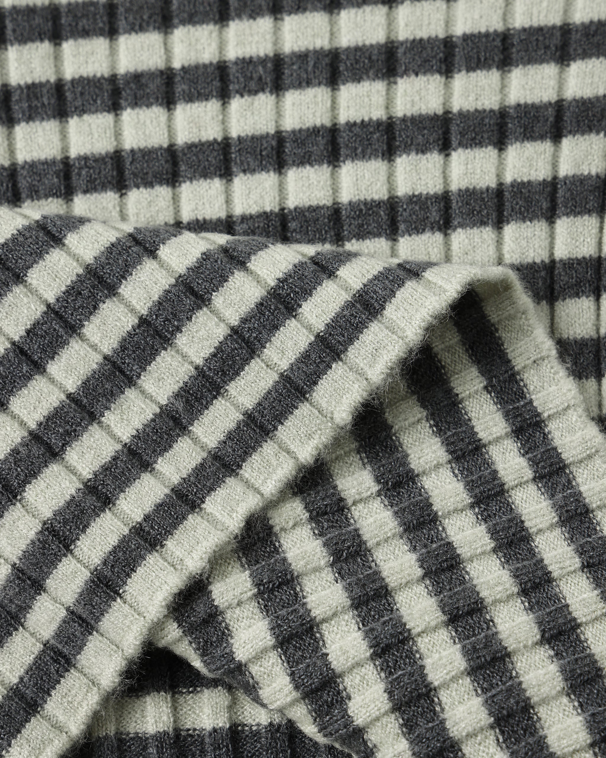 Close-up of a ribbed knit fabric with a dark gray and off-white gingham check pattern, folded to show texture and weave.