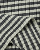 Close-up of a ribbed knit fabric with a dark gray and off-white gingham check pattern, folded to show texture and weave.