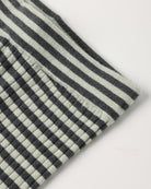 Close-up of a textured fabric with a black and off-white striped pattern and a small stitched pocket on the side, shown on a plain light background.