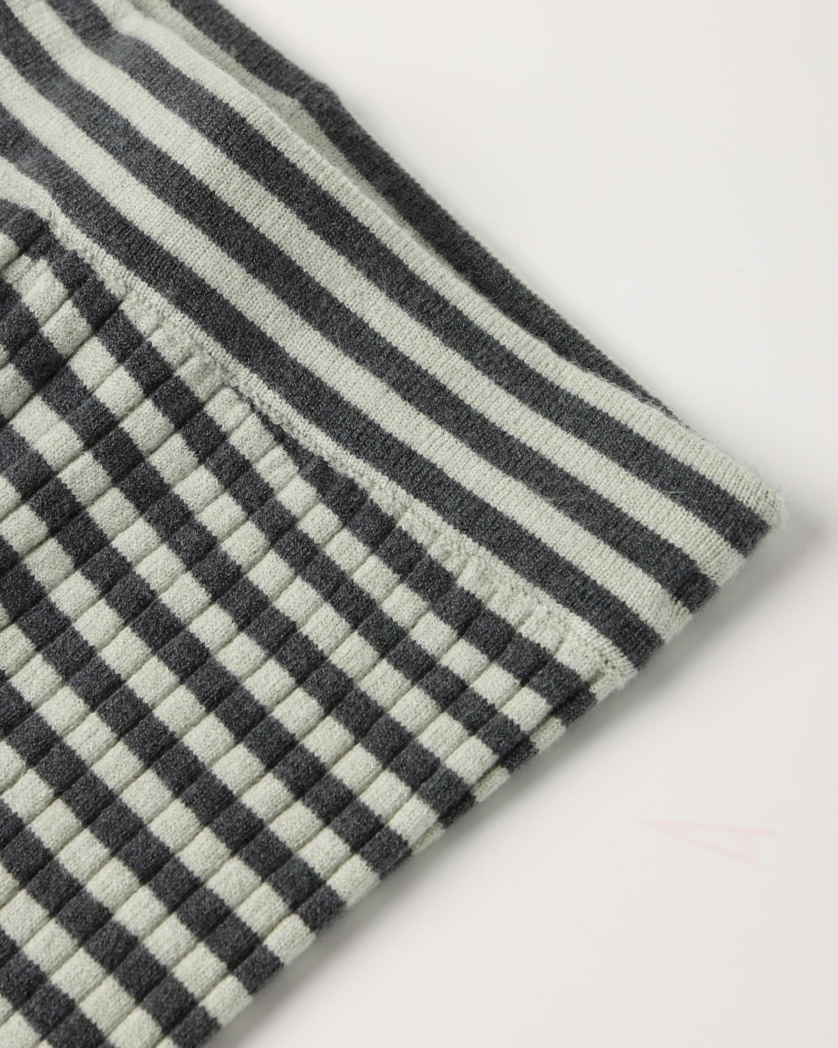 Close-up of a textured fabric with a black and off-white striped pattern and a small stitched pocket on the side, shown on a plain light background.