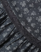 Close-up of a dark gray fabric with a white outline floral and heart pattern, featuring a ruffled trim along the edge.