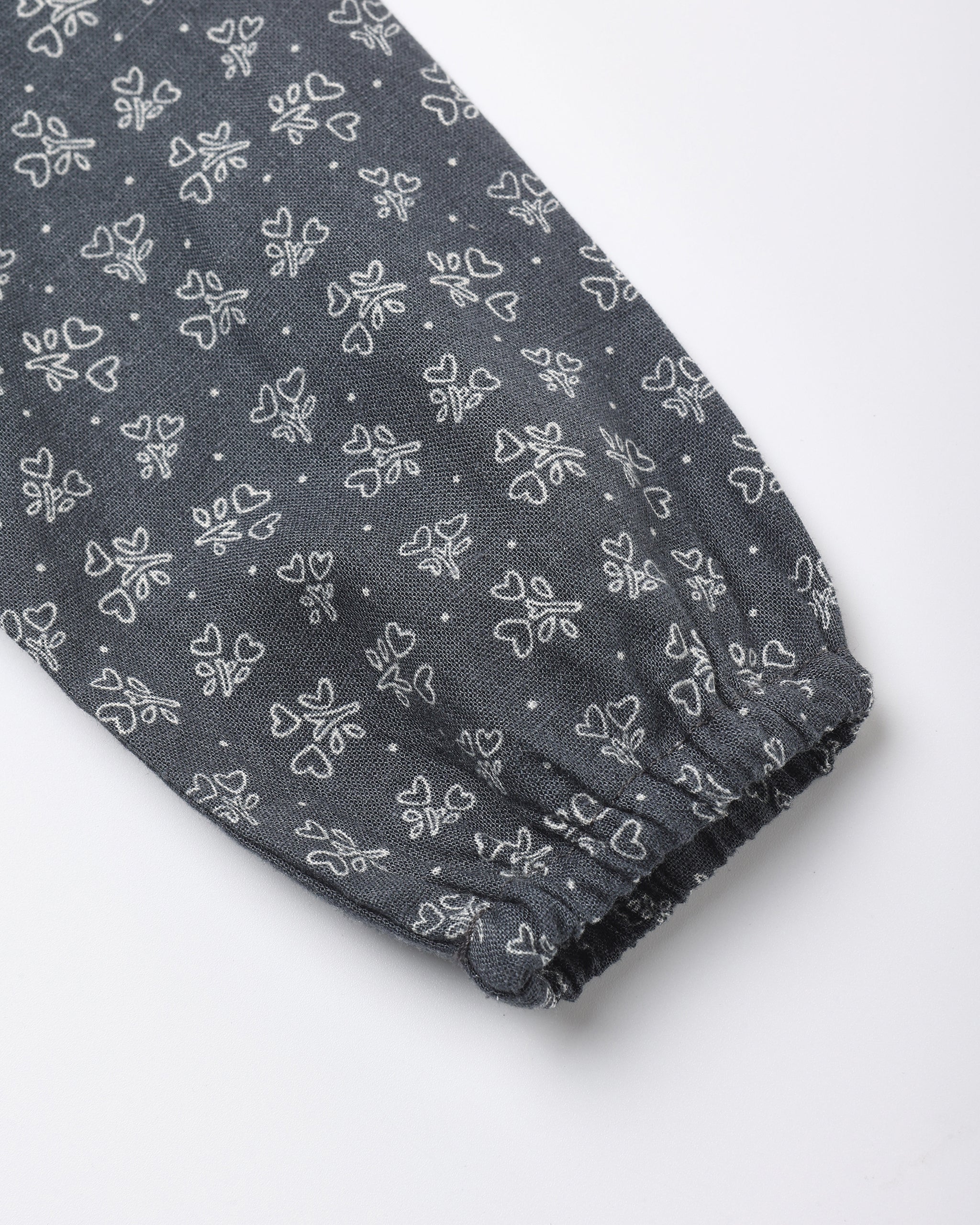 A close-up of a dark gray fabric sleeve or cuff with an all-over white bow and bow print pattern, finished with a gathered elastic hem.